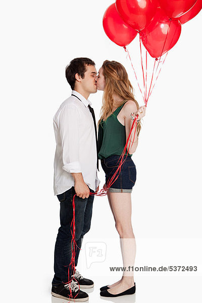 Junges Paar küsst und hält Luftballons vor weißem Hintergrund