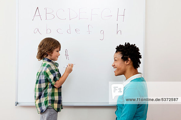 Lehrer und junge Alphabet auf Whiteboard schreiben