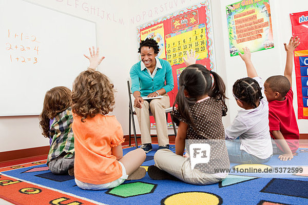 Lehrer und Kinder sitzen mit erhobenen Händen auf dem Boden.