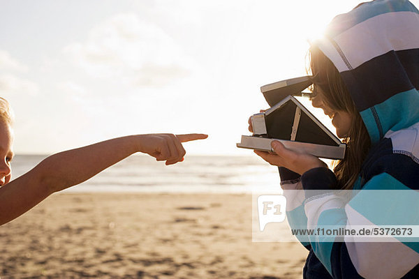 Mädchen zeigt auf Freundin mit Sofortbildkamera am Strand