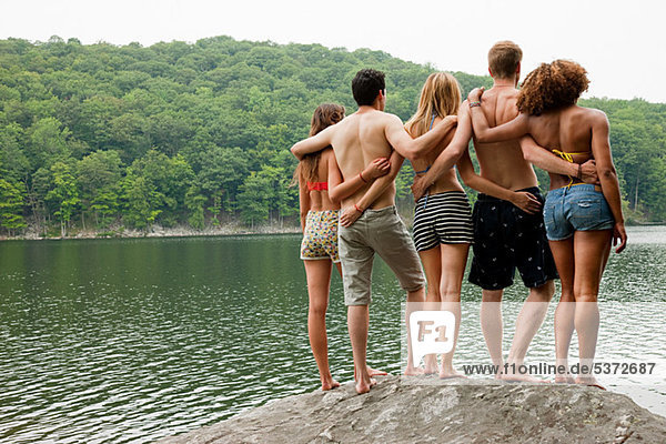 Freunde stehen zusammen auf einem Felsen am Seeufer.