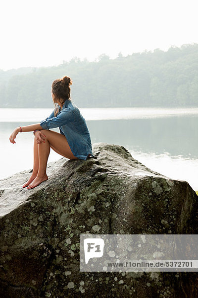 Junge Frau sitzend auf einem Felsen mit Blick auf See