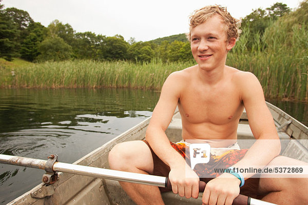 Junger Mann in einem Ruderboot auf einem See während der Sommerferien