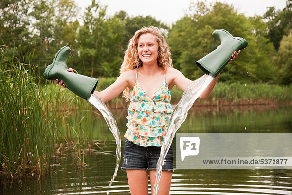 Teenage girl emptying wellies beside lake