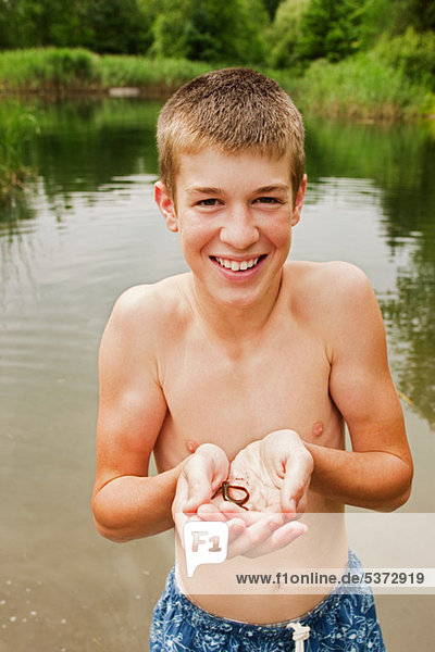 Teenage boy holding small reptile in hands by lake