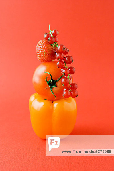 Arrangement aus Pfeffer  Tomaten  Erdbeeren und Johannisbeeren auf orangem Grund