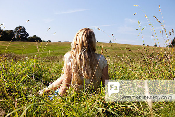 Junge Frau auf einem Feld sitzend mit Rücken zur Kamera