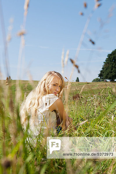 Young Woman sitting in einem Feld  rückwärts Lächeln in die Kamera