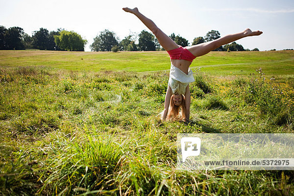 Young woman doing a handstand in a field