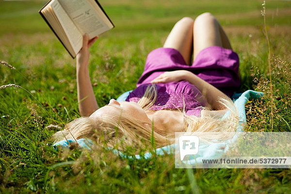 Young woman lying down reading a book in a field