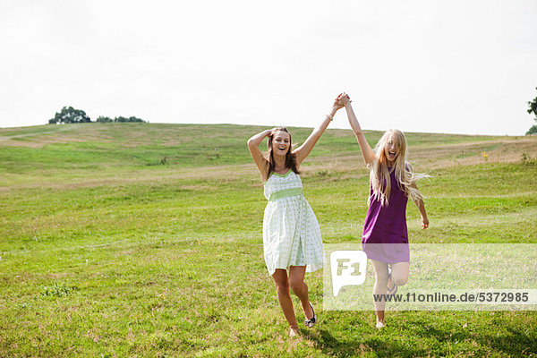 Young women skipping through field with arms raised and hands held