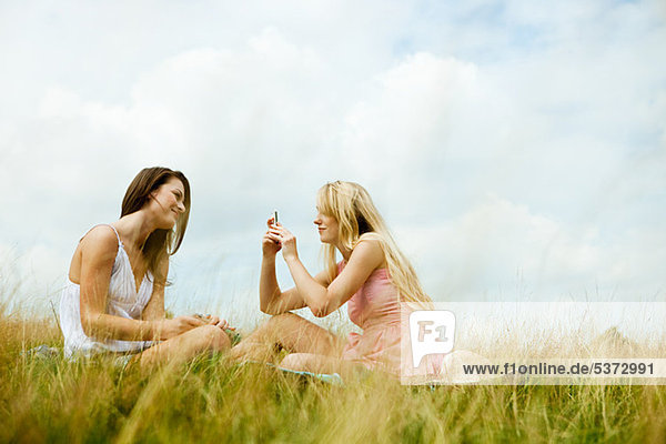 Young women sitting in a field taking a photograph