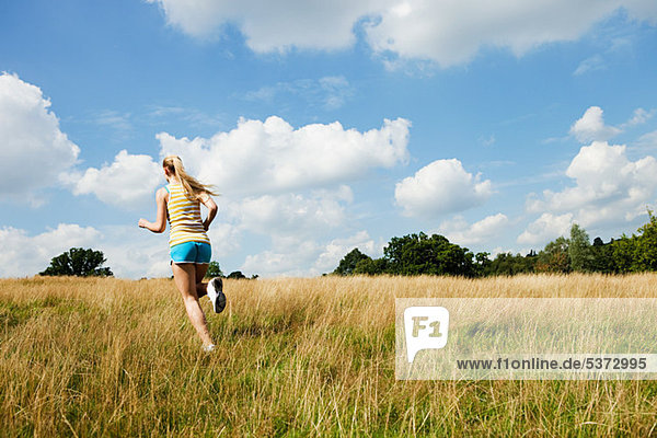 Junge Frau beim Joggen durch ein Feld an einem sonnigen Tag