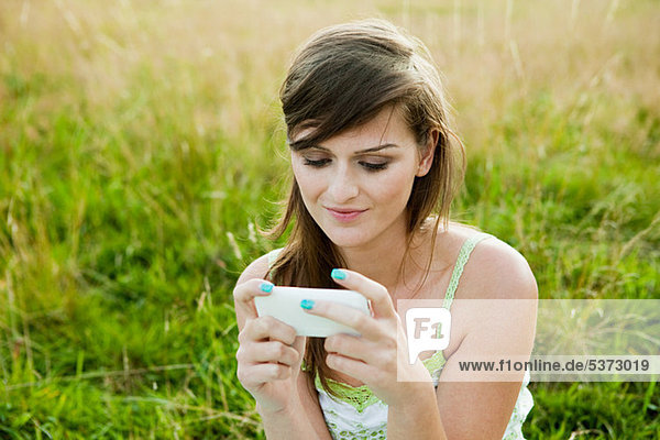 Junge Frau schaut auf ein Handgerät in einem Feld