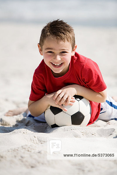Young boy holding football on a beach