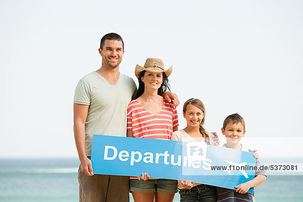 Family holding an airport departures sign on a beach