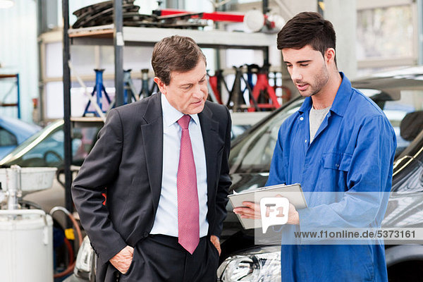 Businessman with car mechanics in repair garage