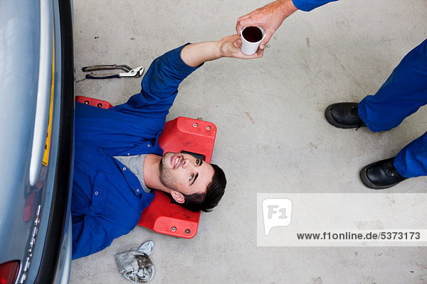Mechanic passing coffee to colleague on floor
