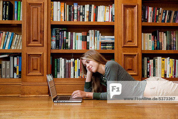 Young Woman using Laptop von Regalen