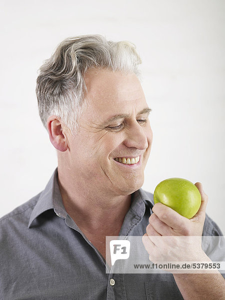 Älterer Mann schaut Apfel an  lächelnd