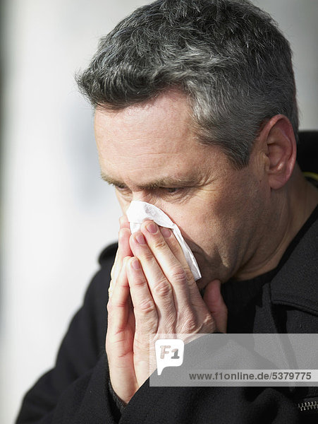 Mature man blowing nose with tissue  close-up