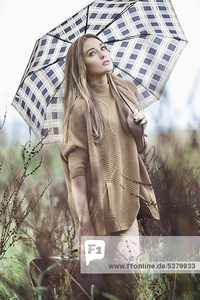 Junge Frau mit Regenschirm und Aktentasche aus Gras