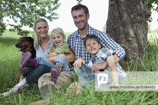 Deutschland  Bayern  Altenthann  Familie mit Hund unter Baum  lächelnd  Portrait