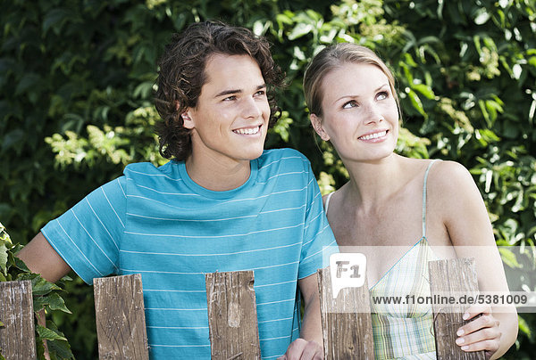 Italien  Toskana  Magliano  Junges Paar hinter Holzzaun stehend  lächelnd