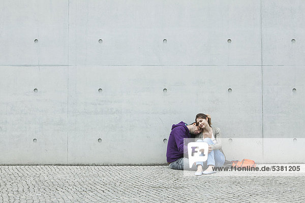 Germany  Berlin  Couple sitting in front of large wall on sidewalk