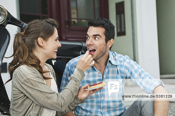 Germany  Berlin  Couple eating snacks on sidewalk