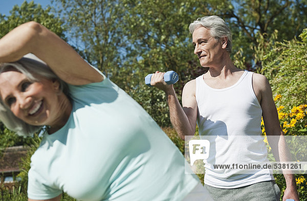 Man lifting dumbells and woman exercising in garden  smiling