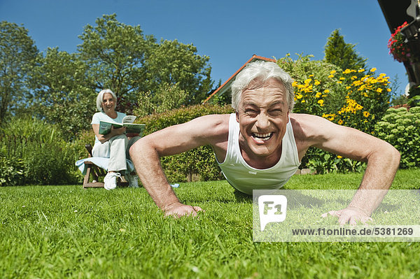 Man exercising and woman reading magazine in garden  smiling