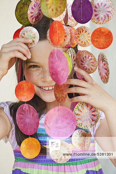 Mädchen schaut durch dekorative Muscheln Windspiel