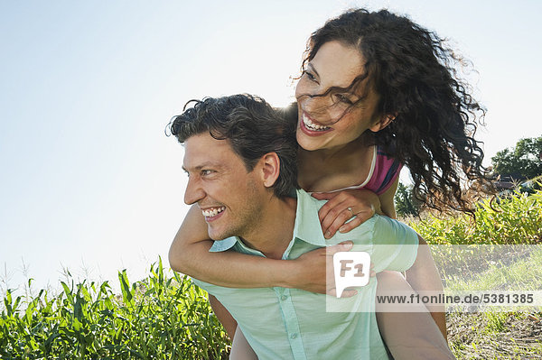 Mann mit Frau auf dem Rücken  lächelnd
