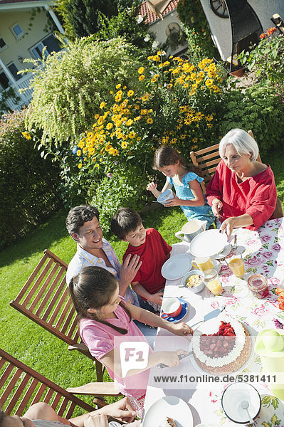 Germany  Bavaria  Family having coffee and cake in garden  smiling