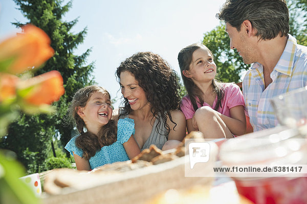 Germany  Bavaria  Family having coffee and cake in garden  smiling