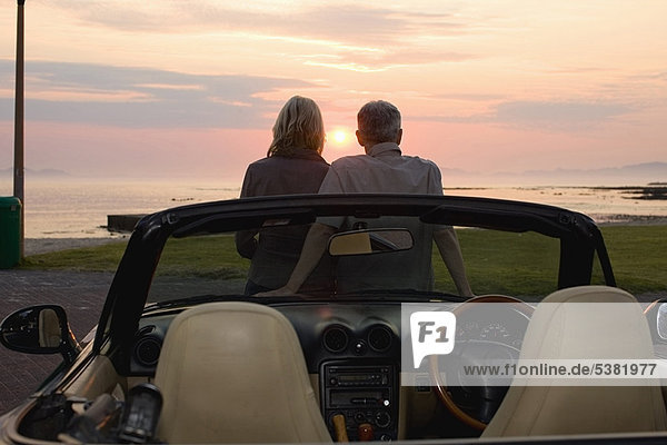 Paar bewundert Sonnenuntergang im Cabriolet