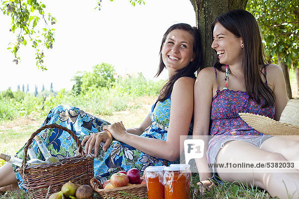 Lächelnde Frauen picknicken im Obstgarten