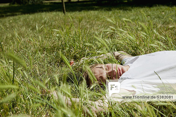 Teenager-Junge im hohen Gras liegend