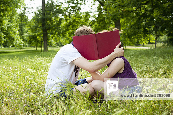 Teenager verstecken sich hinter einem Buch im Park