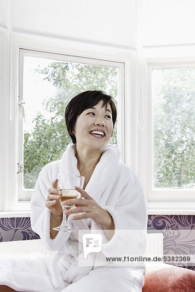 Woman in bathrobe drinking glass of wine