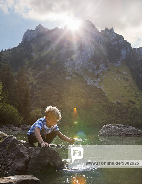 Boy dipping mug into still lake