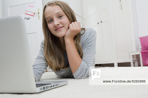 Smiling girl using laptop on floor