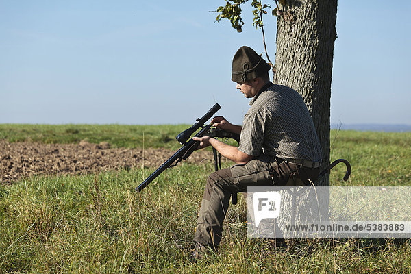 Hunter sitting on his portable hunting spike seat and loading his rifle
