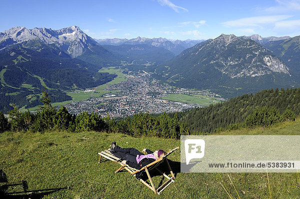 Junge Frau im Liegestuhl  Blick vom Wank auf Garmisch-Partenkirchen mit Zugspitze  Jubiläumsgrat und Alpspitze  Oberbayern  Bayern  Deutschland  Europa