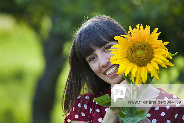 Junge Frau  25 Jahre  hält Sonnenblume vor ihr Gesicht
