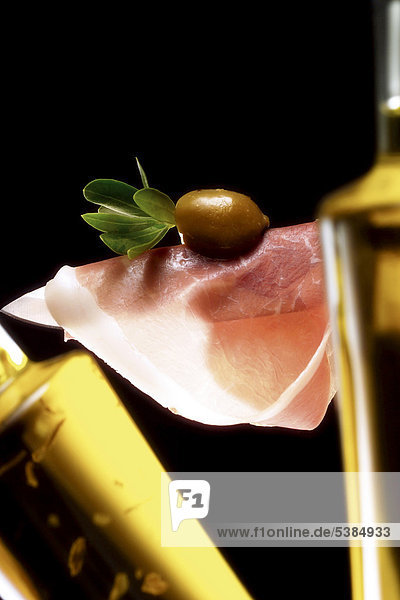 Eine Scheibe roher Schinken auf Messerklinge mit Olive