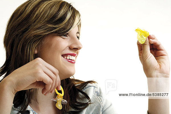 Junge Frau schaut lächelnd auf ein Kondom und hält einen Schnuller in der anderen Hand - Symbol Kind oder Karriere