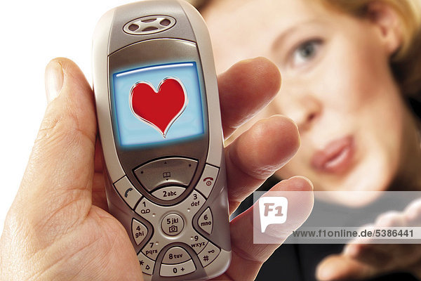 Hand hält Handy mit Herzlogo  im Hintergrund eine junge Frau - Symbol für Liebes-SMS