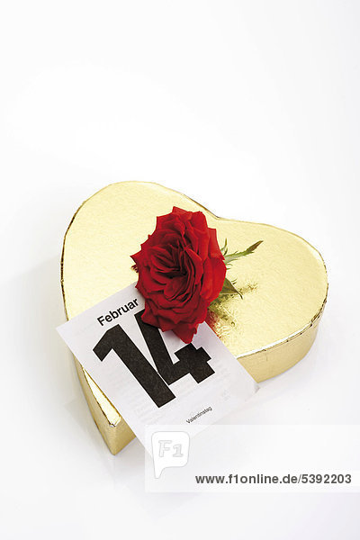 Goldenes Geschenkpäckchen in Herzform mit roter Rose und Kalenderblatt 14. Februar - Valentinstag